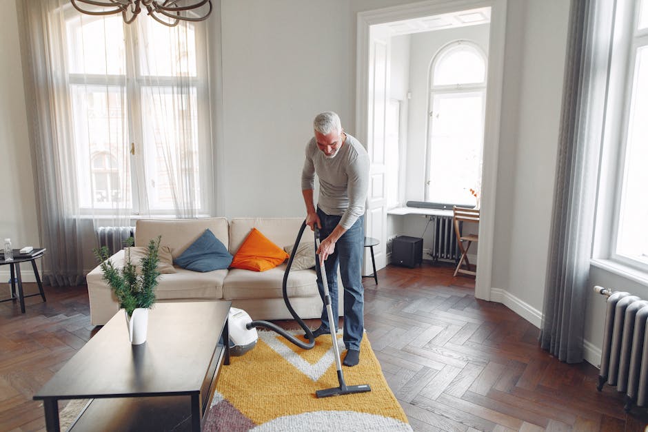 A person, likely using a commercial cleaning device, holds a yellow portable carpet or surface cleaning machine with a black vented front panel. The individual’s hands are positioned on the device, 